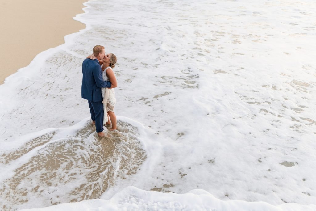 Eloping couple standing in the ocean with the foam swirling around them