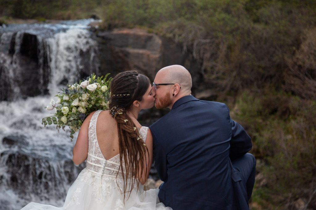 eloping couple kissing in front of a waterfall