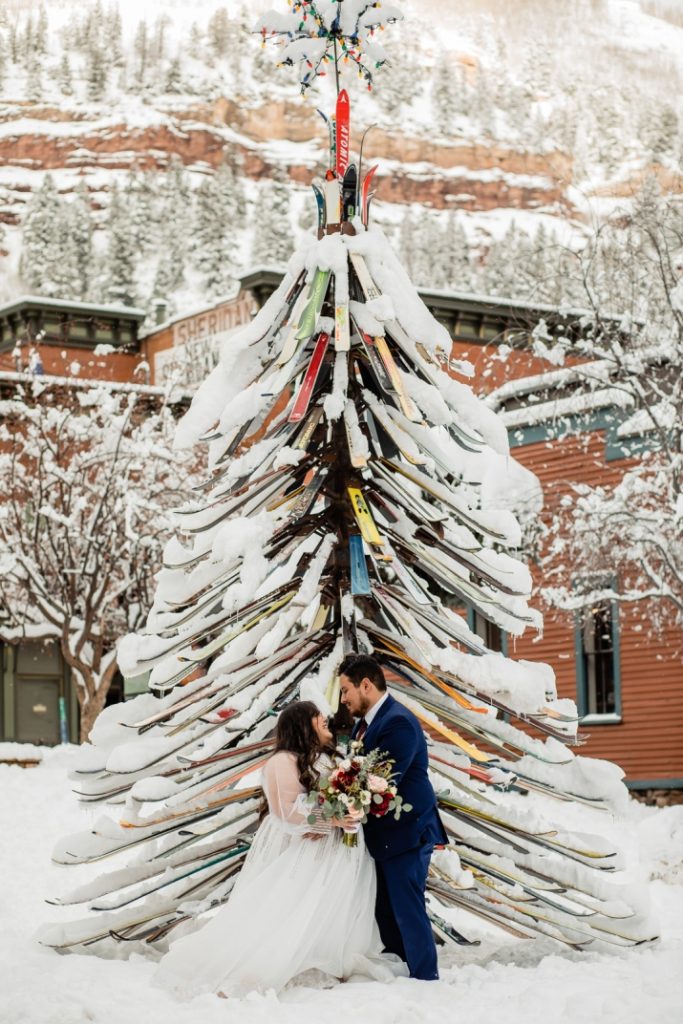 bride and groom in front of snow-covered Christmas tree in Telluride